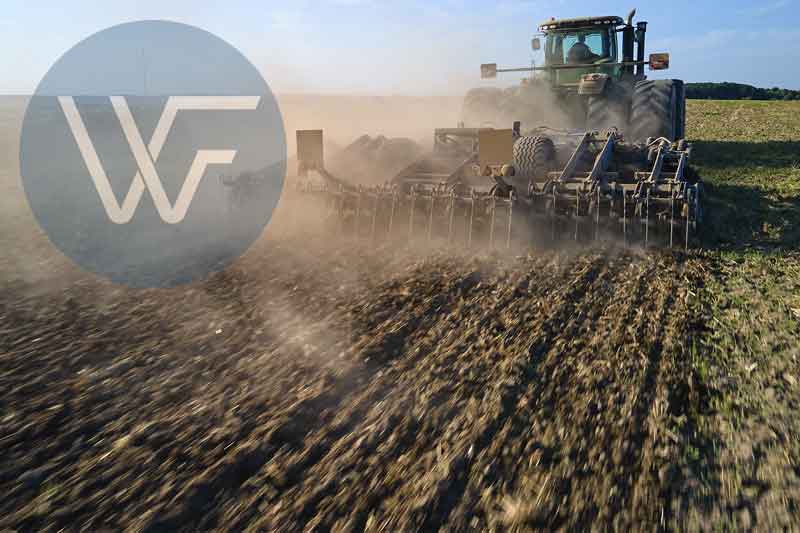 Tractor tilling soil in an agricultural field with dust being kicked up.