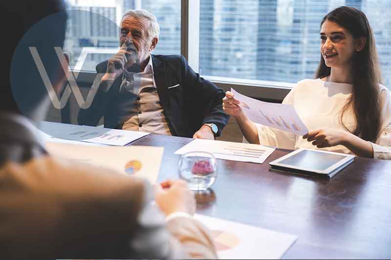 Two individuals engaged in a business meeting, one presenting charts and graphs while another listens attentively.