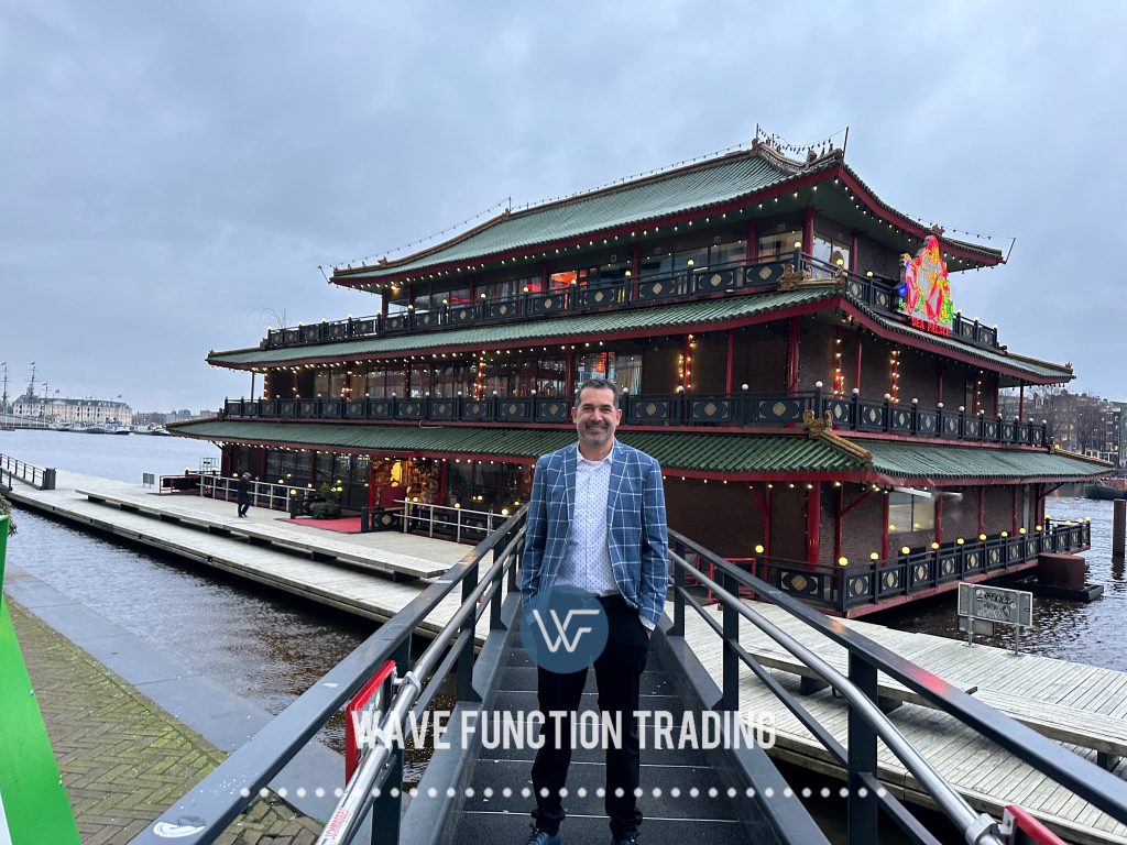 A man in a checked blazer standing on a walkway in front of a Chinese restaurant by the water.