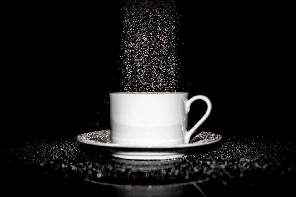 Dynamic black and white image of sugar pouring into a white cup on a saucer against a black background.