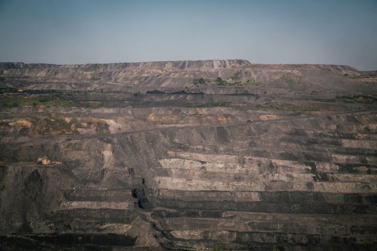 A vast open-pit coal mine under a clear blue sky, showcasing industrial landscape and natural rock formations.