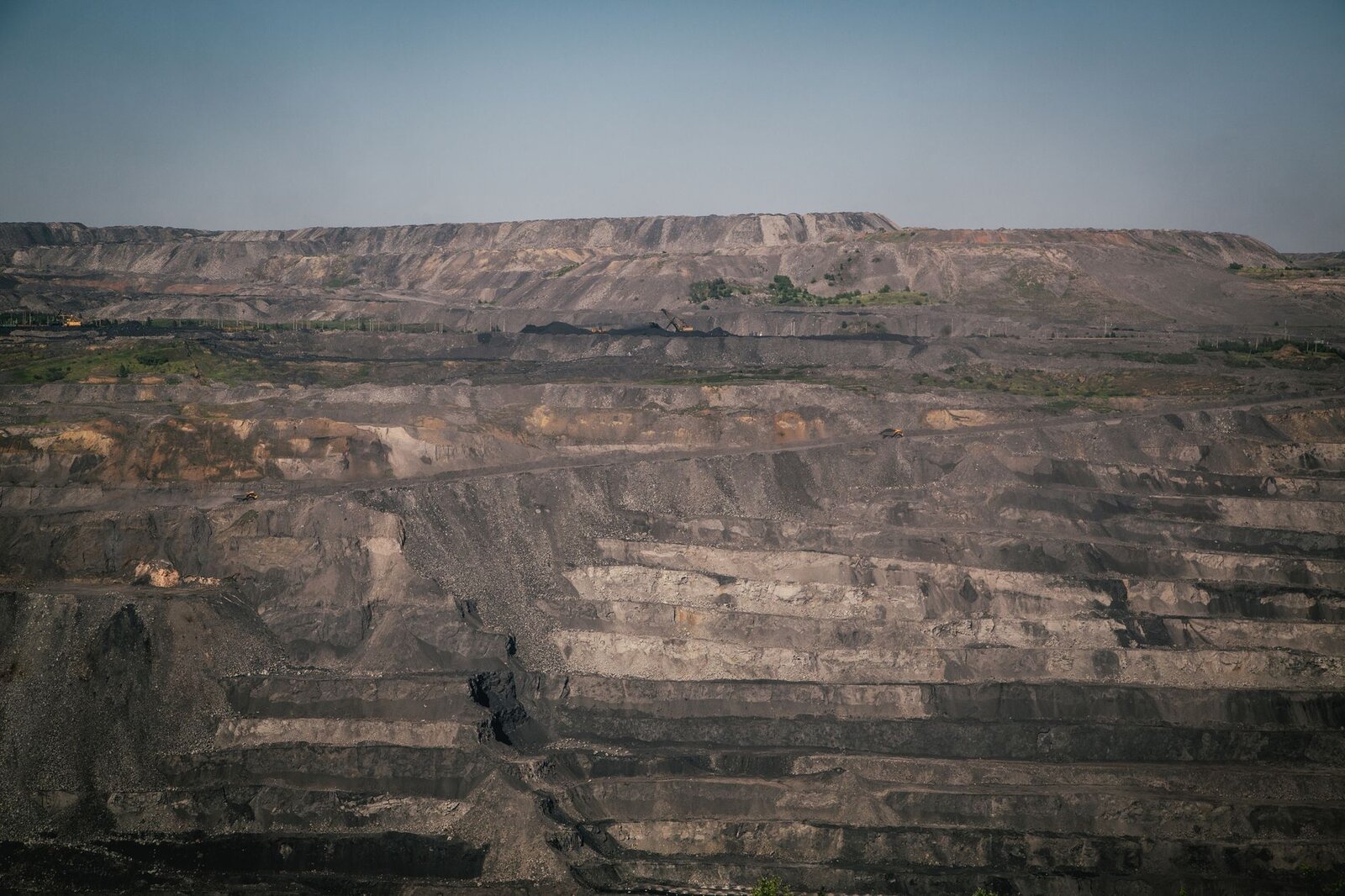 A vast open-pit coal mine under a clear blue sky, showcasing industrial landscape and natural rock formations.