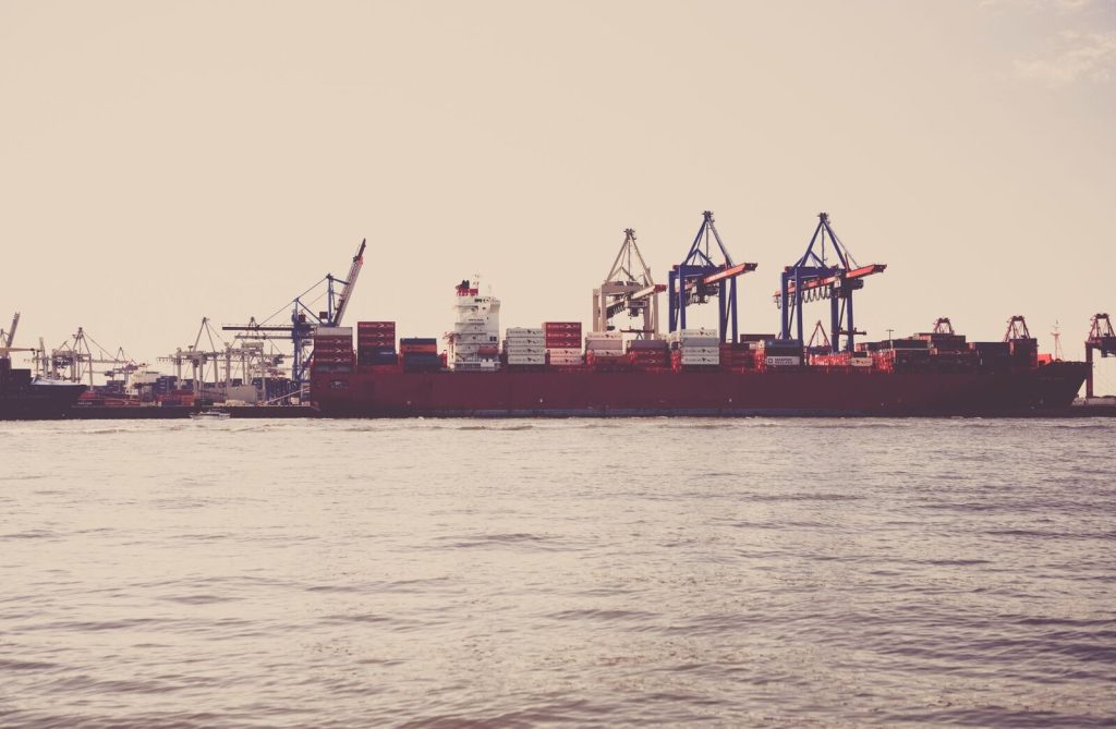 A cargo ship loaded with containers docked at a seaport under clear skies.