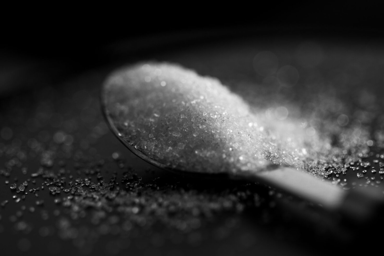 Artistic black and white close-up of sugar crystals on a spoon with dramatic lighting.