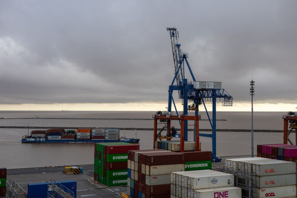 Large cargo cranes at a shipping port with stacked containers and cargo ship.
