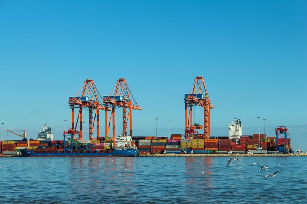 Colorful container port with large cranes and ships against a clear blue sky.