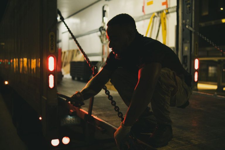 Man securing chains on a cargo truck at night in Houston, Texas.