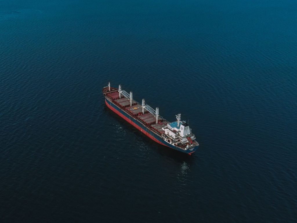 An aerial shot of a cargo ship navigating the open sea, surrounded by deep blue water.