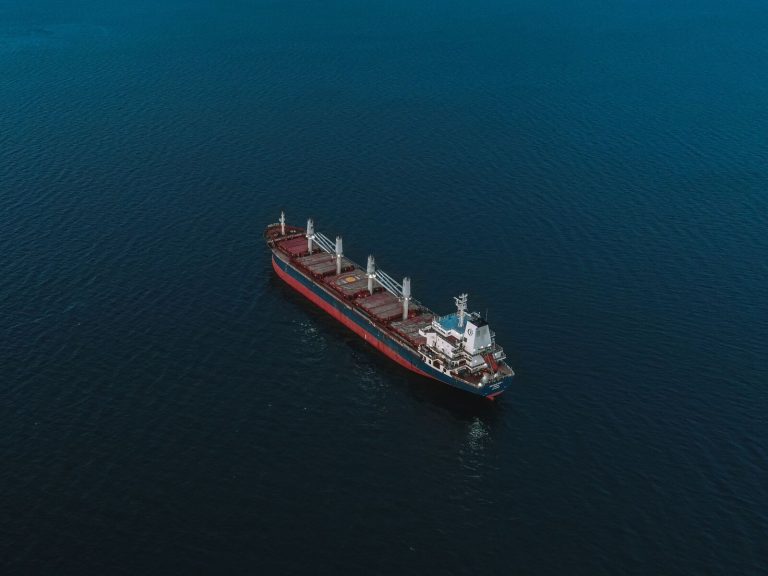 An aerial shot of a cargo ship navigating the open sea, surrounded by deep blue water.
