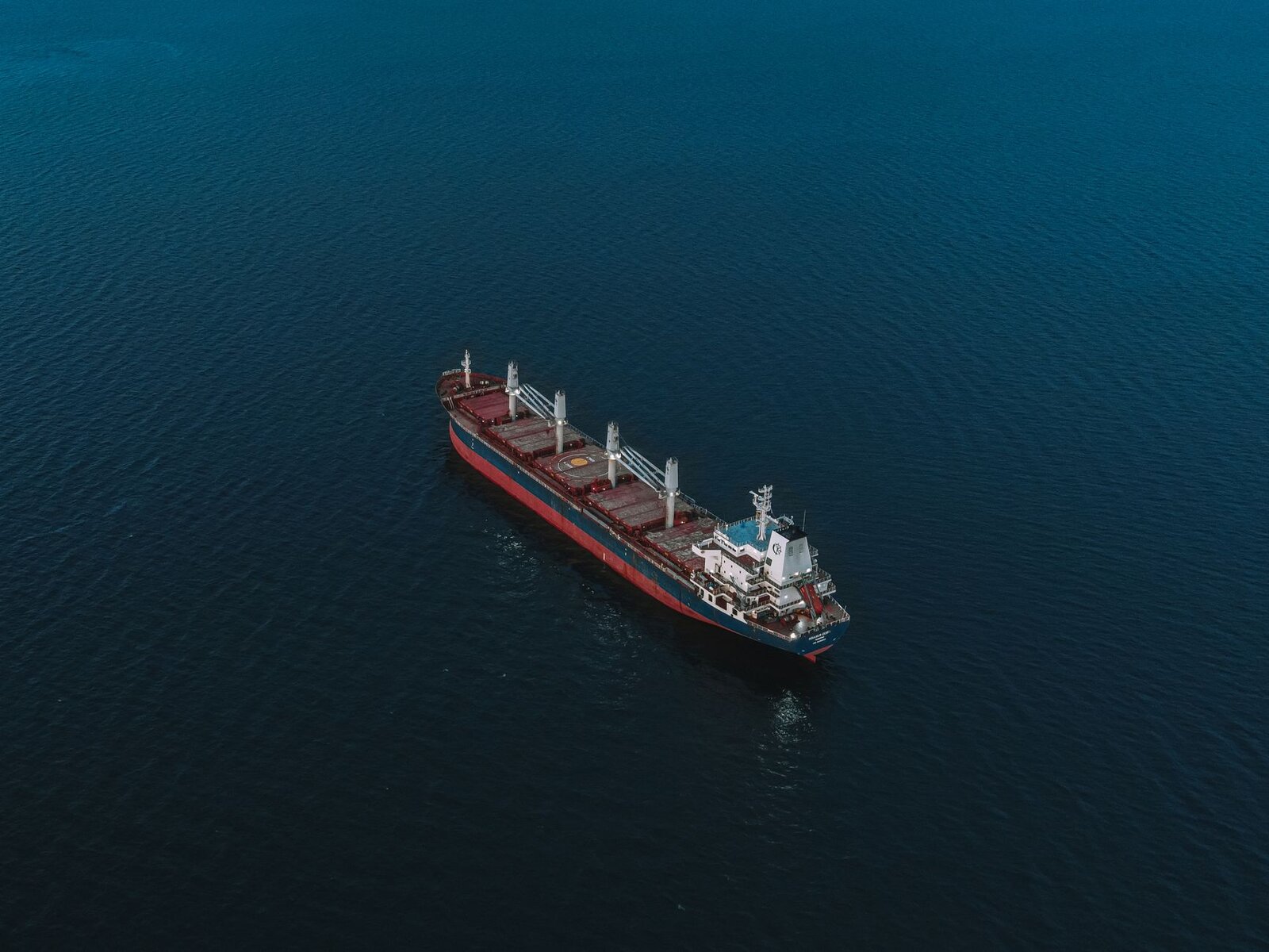 An aerial shot of a cargo ship navigating the open sea, surrounded by deep blue water.