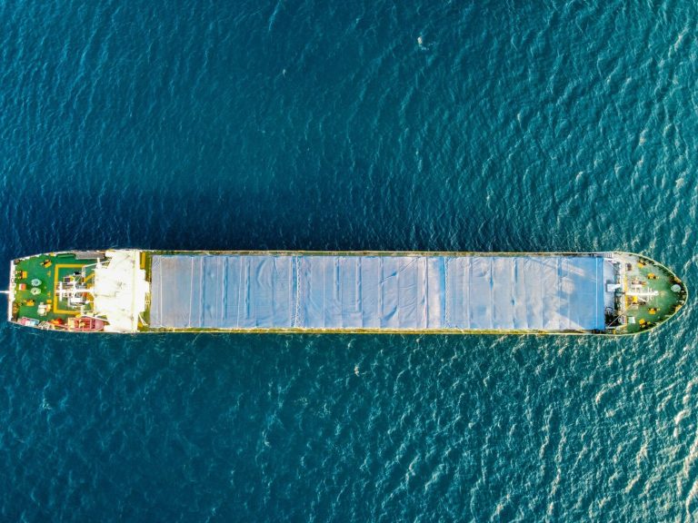 Top-down aerial view of a cargo ship navigating the open sea under clear skies.