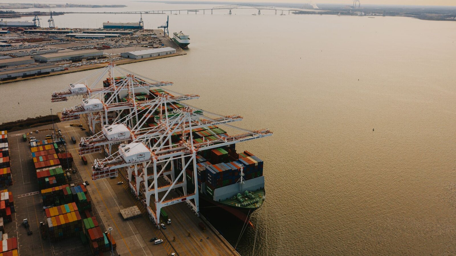 Drone view of cargo containers loaded on long ship on river of pier with lifting cranes