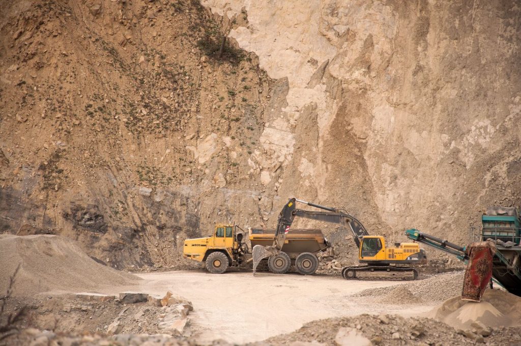 Industrial excavator with bucket and tracks digging ground while extracting minerals near rocky formations in quarry with machines and special equipment
