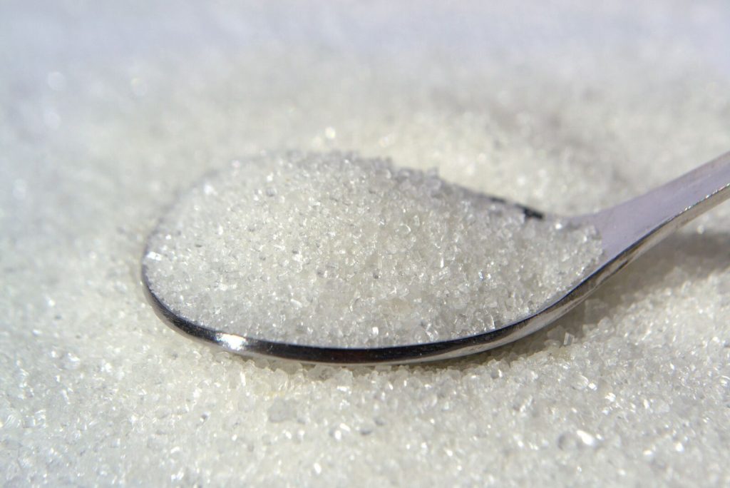 Macro shot of white sugar crystals on a stainless steel spoon, highlighting texture and purity.
