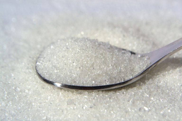 Macro shot of white sugar crystals on a stainless steel spoon, highlighting texture and purity.
