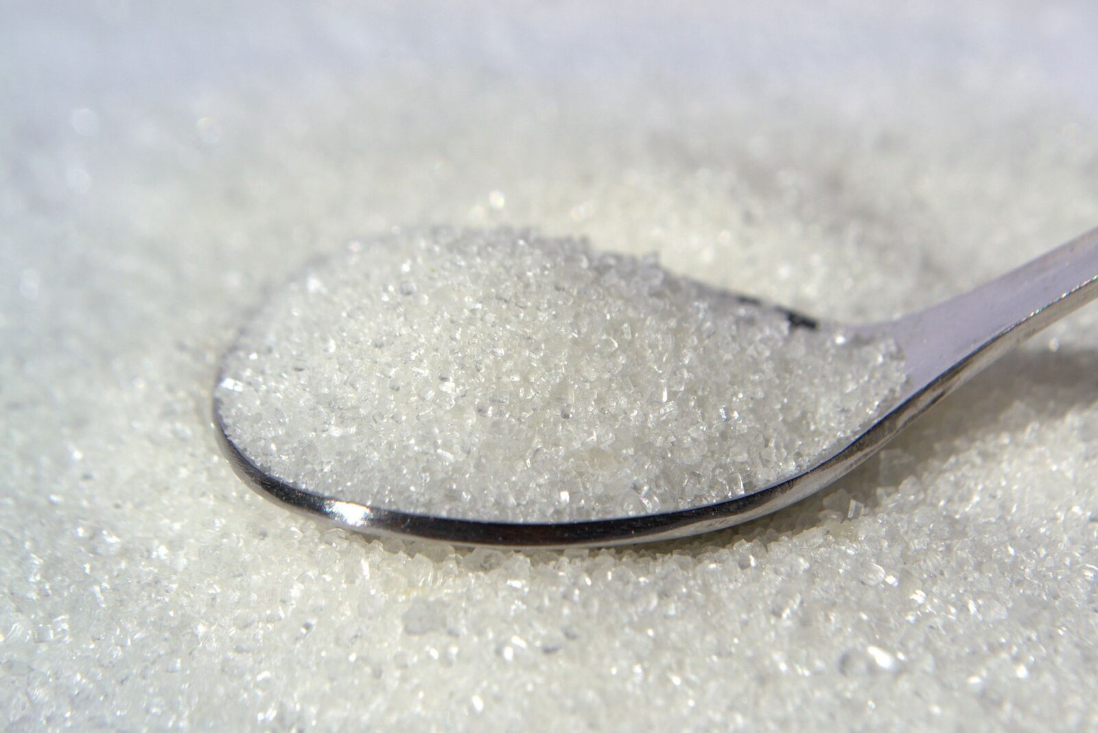 Macro shot of white sugar crystals on a stainless steel spoon, highlighting texture and purity.