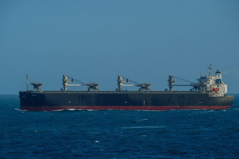 A large cargo ship sails through a vast, calm blue ocean under a clear sky, capturing maritime travel.