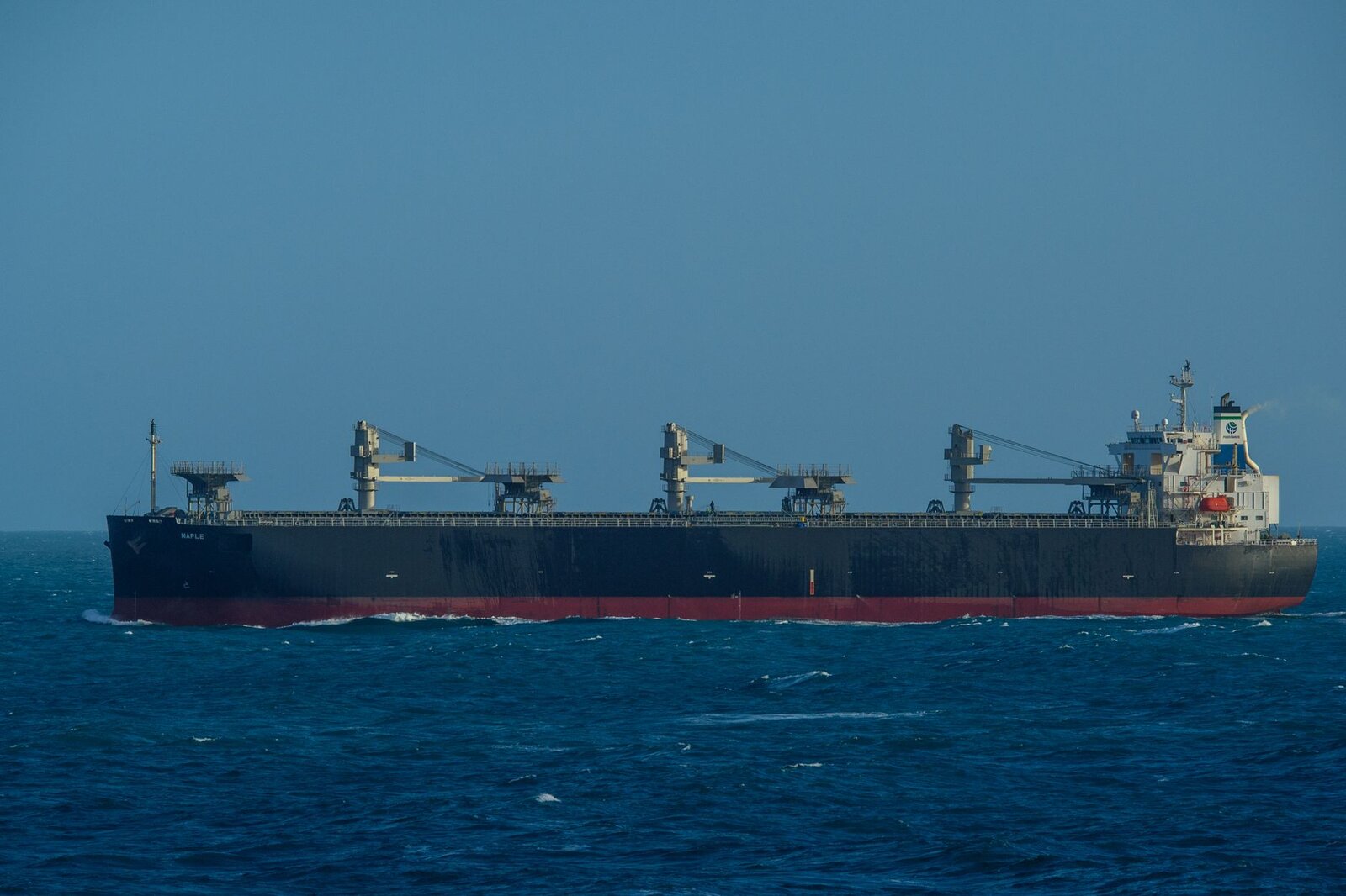 A large cargo ship sails through a vast, calm blue ocean under a clear sky, capturing maritime travel.