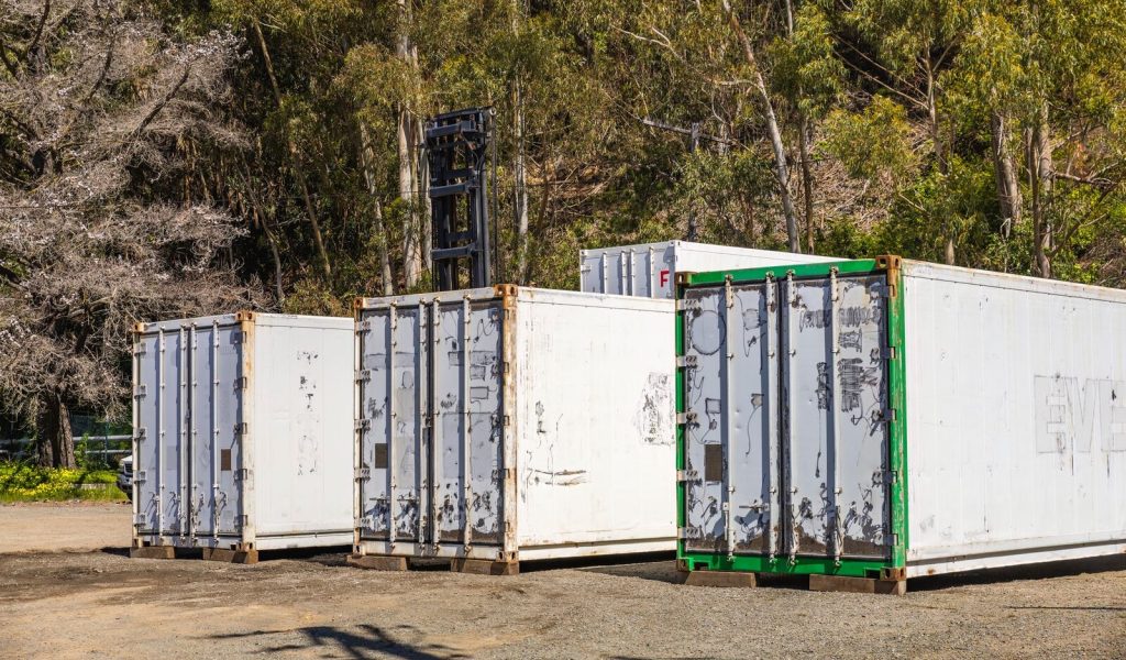 Group of white shipping containers set against a forest backdrop, illustrating transportation logistics.