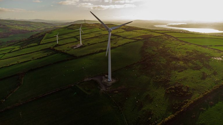 Scenic aerial view of wind turbines in rolling green fields at sunset, promoting renewable energy and sustainability.