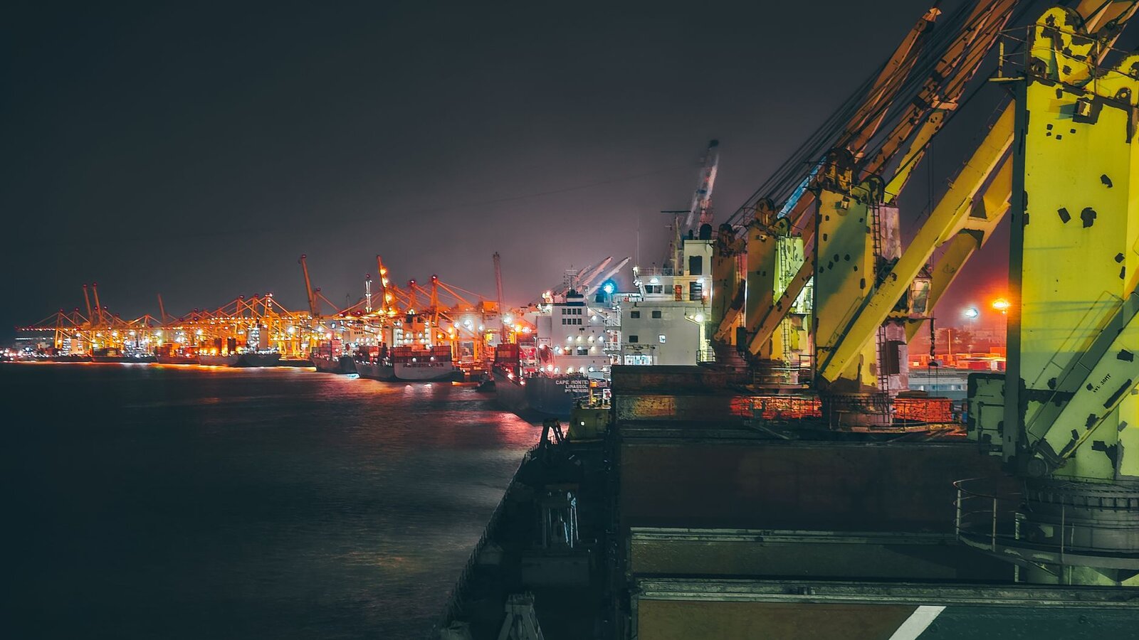 Cargo ships illuminated at night in a bustling harbor showcasing logistics and maritime activity.