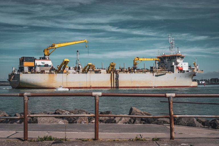 A large cargo ship with cranes docked at Rostock harbor on a sunny day, showcasing maritime logistics.