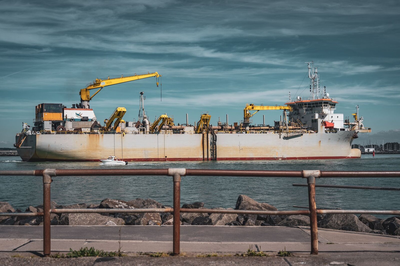 A large cargo ship with cranes docked at Rostock harbor on a sunny day, showcasing maritime logistics.