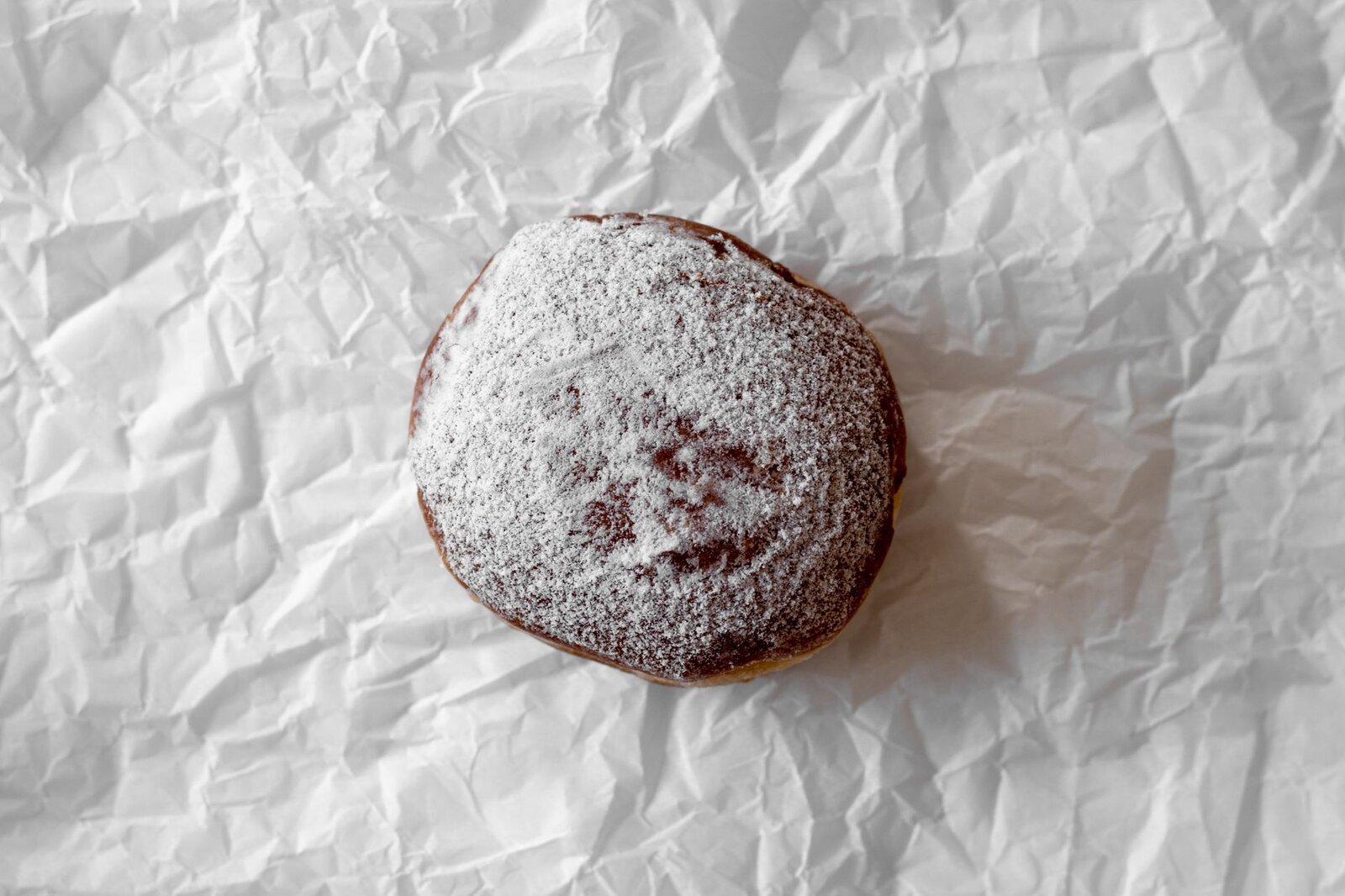 A tempting sugar-dusted doughnut resting on crumpled paper, ideal for food photography.