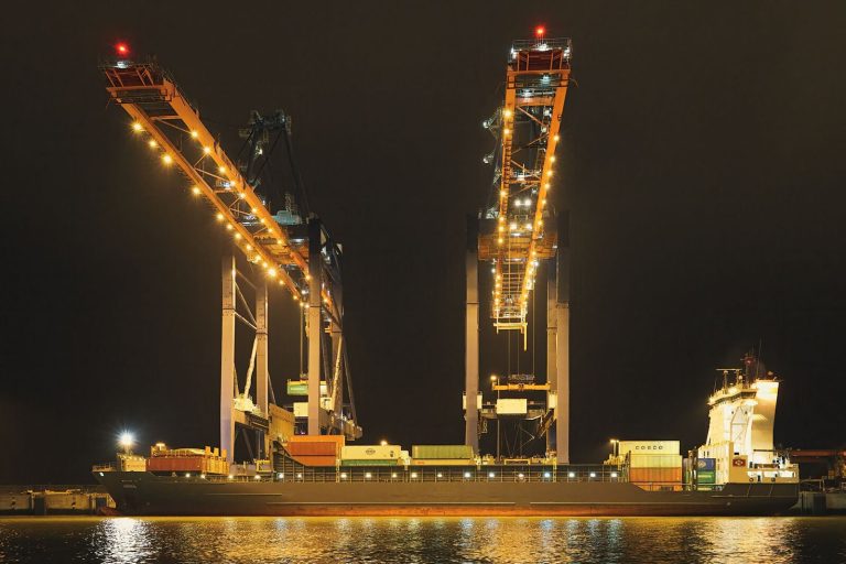 Container ship docked in Rotterdam Harbor illuminated by cranes at night, showcasing industrial infrastructure.