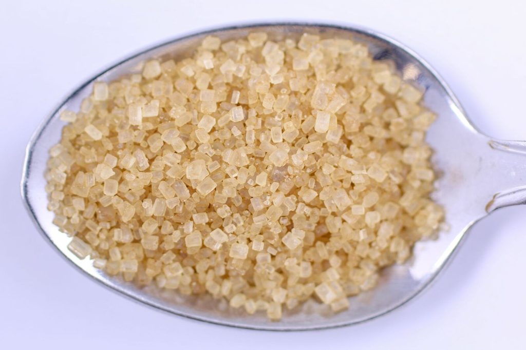 Detailed close-up of raw brown sugar on a metal spoon, perfect for food and cooking themes.