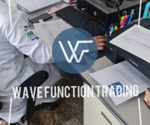 Individual seated at a desk using a computer with papers and office supplies visible.