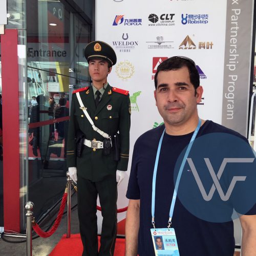 A man standing next to a uniformed guard at an entrance to an event, with branding in the background.